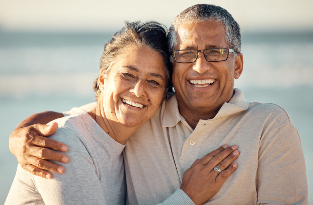 Closeup portrait of an senior affectionate mixed race couple standing on the beach and smiling during sunset outdoors. Hispanic couple showing love and affection on a romantic date at the beach